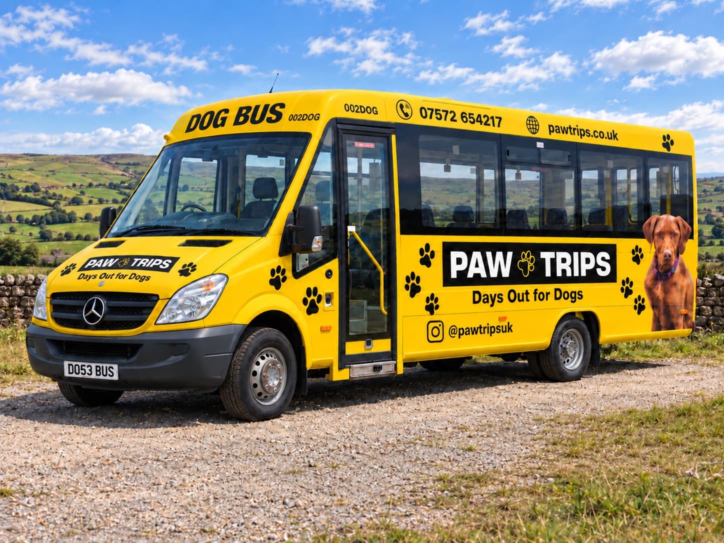 The yellow PawTrips bus from the front three-quarter, parked on a gravel track with the fells behind